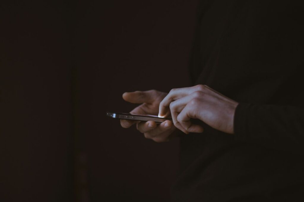Homem, vestido com um terno preto, segurando um celular nas mãos.