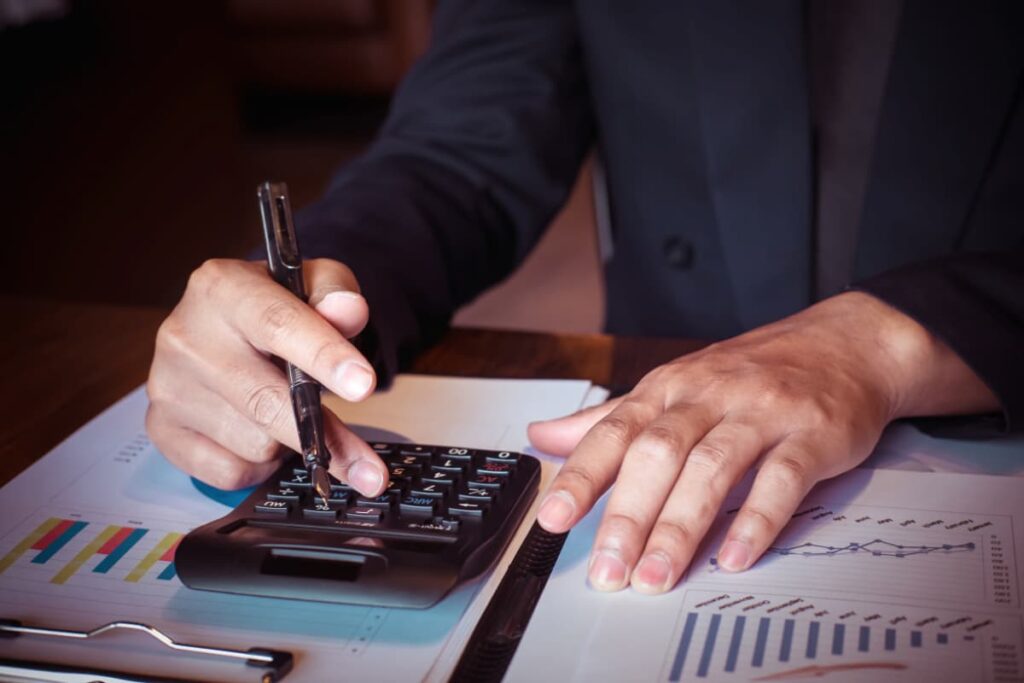 Uma pessoa realizando uma auditoria de contas, utilizando uma calculadora e analisando gráficos e documentos financeiros.