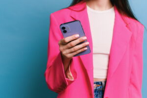 Pessoa em blazer rosa segurando um smartphone, representando que um celular corporativo pode ser monitorado.