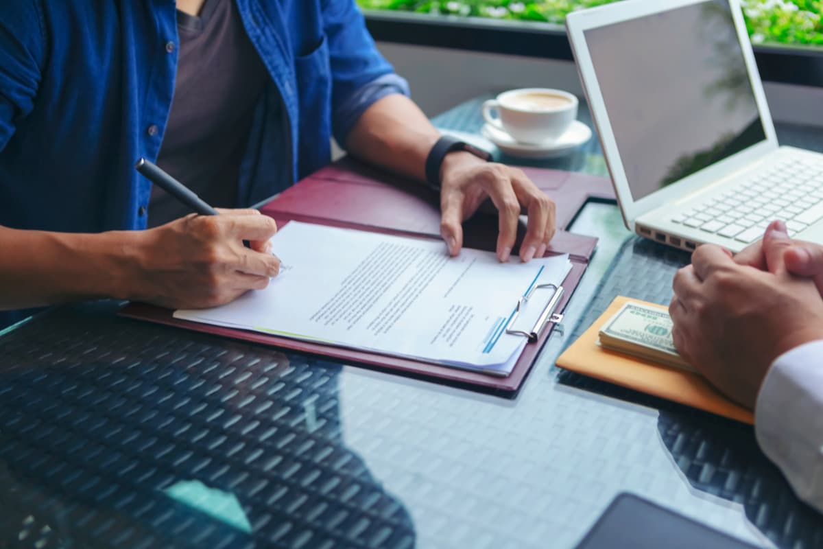 Duas pessoas em reunião com documentos e laptop, discutindo a renegociação de contrato.