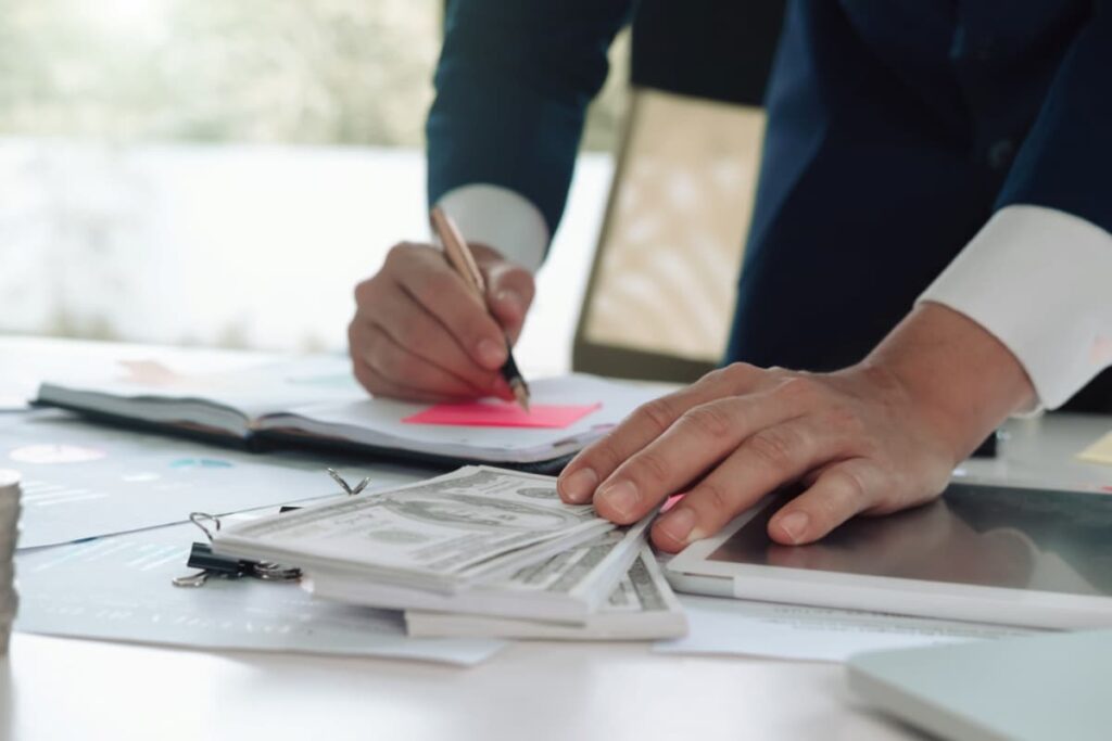 Mãos escrevendo em documento, representando estratégias para reduzir custos da empresa.