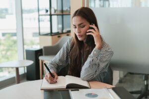 Mulher de negócios discutindo planos de telefone para empresas, com gráficos e notebook na mesa.