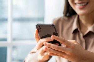 Mulher sorrindo enquanto usa dados móveis em seu smartphone, em um ambiente iluminado pela luz natural.