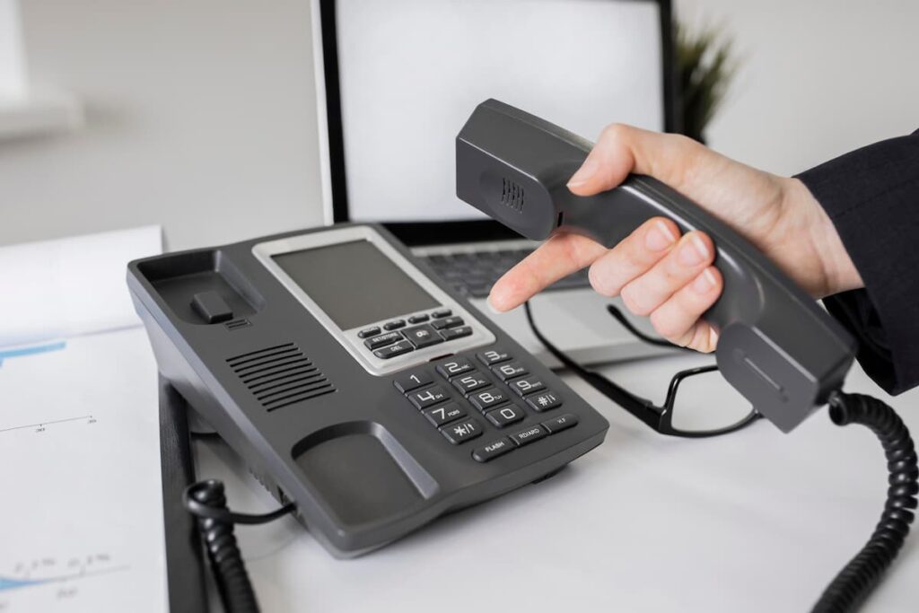 Pessoa segurando o fone de um telefone IP em um escritório, representando o uso da tecnologia VoIP para comunicação.