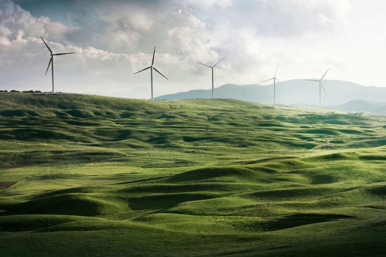 Aerogeradores mostrados ao longe, sobre um campo verde, representando a energia aeólica.