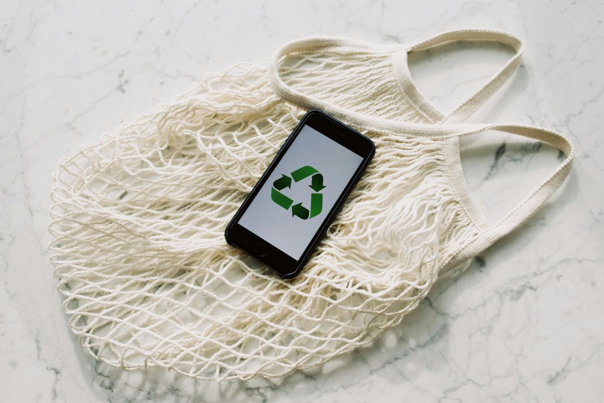 Sacola sustentável, com um celular sobre ela. No celular há o símbolo da reciclagem.