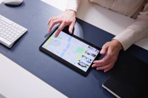 Pessoa configurando um geofence em um tablet, visualizando um mapa em uma mesa de escritório com teclado e caderno ao lado.