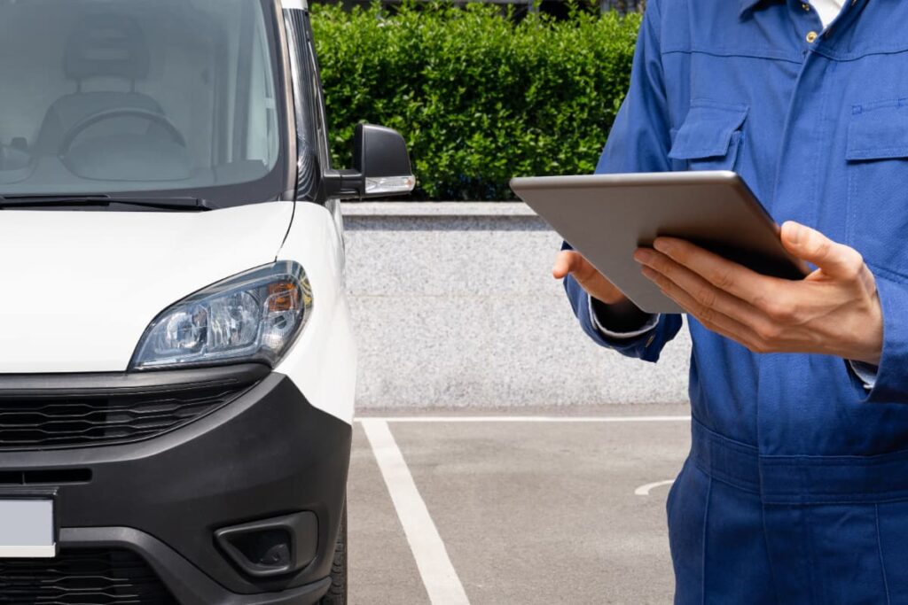 Profissional utilizando tablet para realizar a gestão de frotas ao lado de um veículo comercial estacionado.