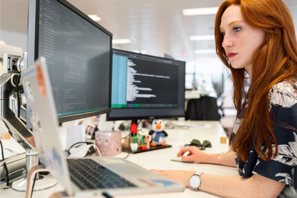 Mulher trabalhando em um NOC (Centro de Operações de Rede), monitorando sistemas e redes em múltiplos monitores.