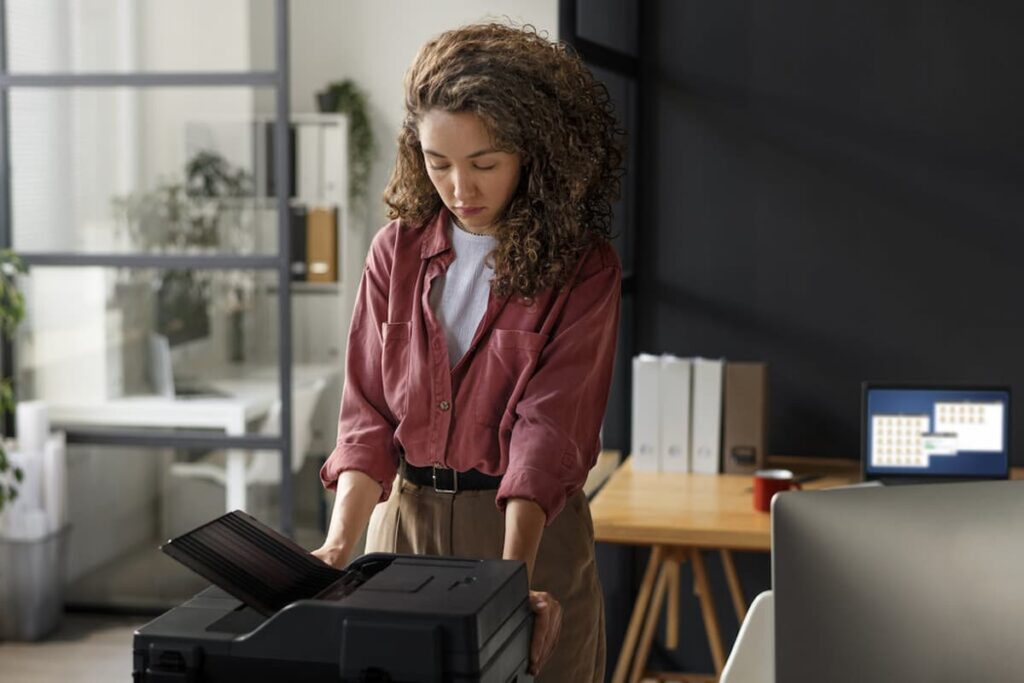 Mulher operando uma impressora em um escritório, representando o conceito de gerenciamento de impressão eficiente.