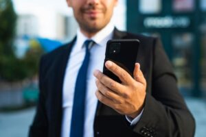 Homem em terno segurando um smartphone, representando um perfil de trabalho Android.