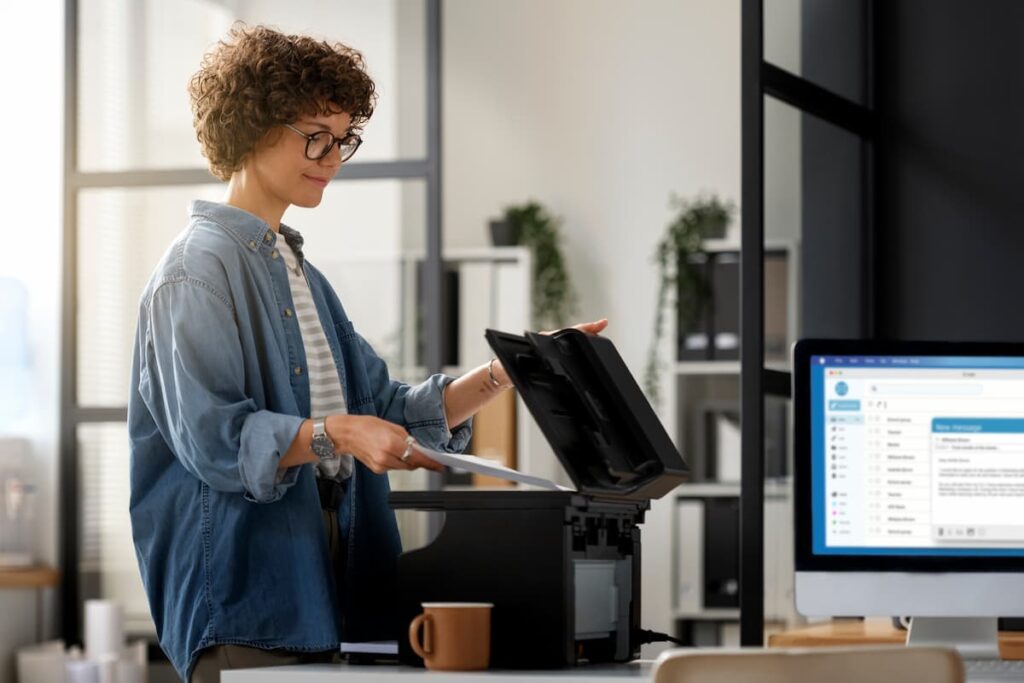 Mulher usando impressora em escritório moderno, representando a eficiência do outsourcing de impressão em ambientes corporativos.