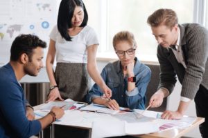 Time em escritório corporativo, com diversos documentos e dados sobre a mesa, discutindo sobre essas informações.