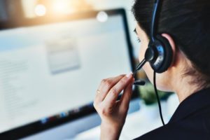 Mulher usando um headset em frente a um monitor de computar realizando atendimento de telemarketing.